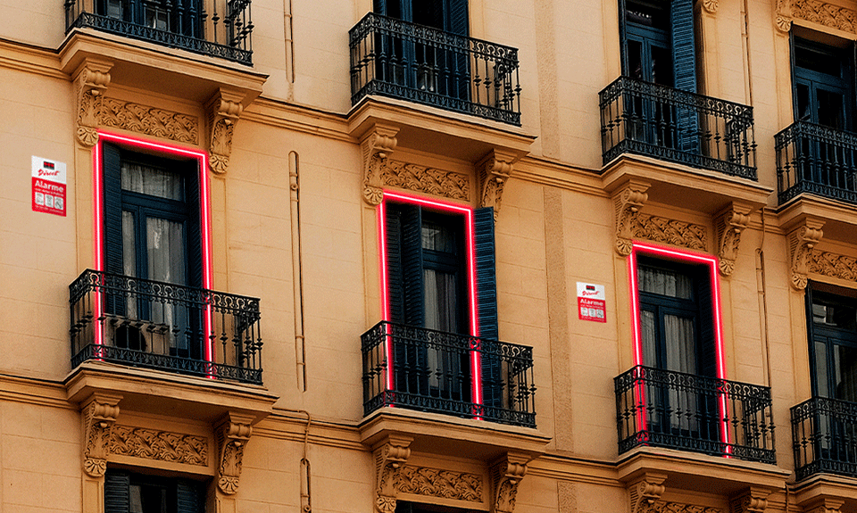 • Fachada de um edifício neo-clássico com janelas iluminadas e placa dissuasora do alarme da Securitas Direct, destacando a proteção contra intrusões para residências.