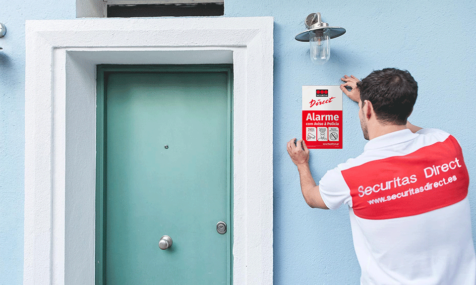 • Técnico da Securitas Direct fixando uma placa de alarme ao lado de uma porta de entrada de uma vivenda, garantindo proteção contra roubos e invasões.